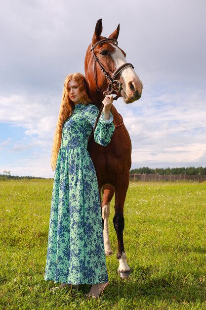 Orange hair woman and her brown horse in the field just relaxing in summer day