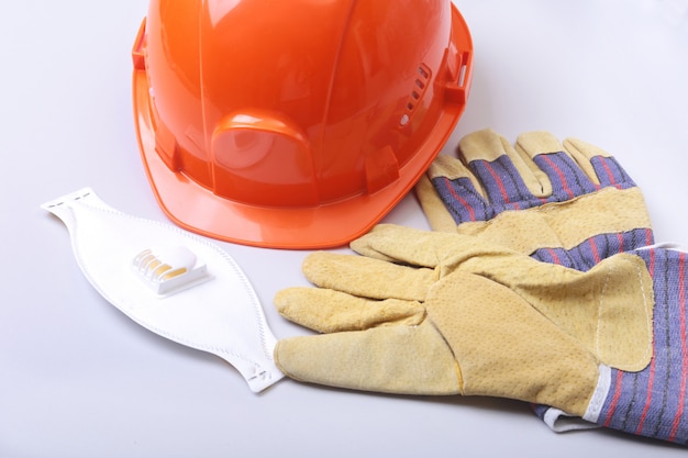 Orange hard hat, goggles, protective mask, respirator and safety gloves on a white background.