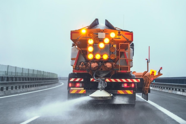 Orange highway maintenance gritter truck spreading de-icing salt on road in winter.