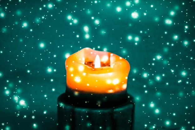 Photo orange holiday candle on green sparkling snowing background luxury branding design for halloween new years eve and christmas