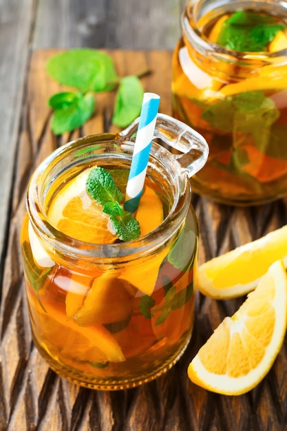 Orange iced tea with mint leaves in a glass jar on the old wooden surface. Selective focus.