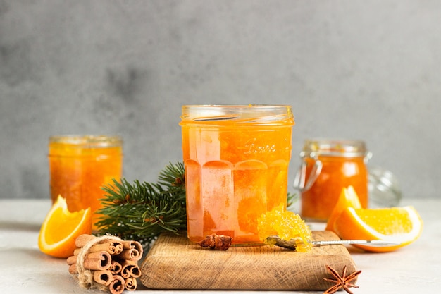 Orange jam in a glass jar with winter spices and fir branches.