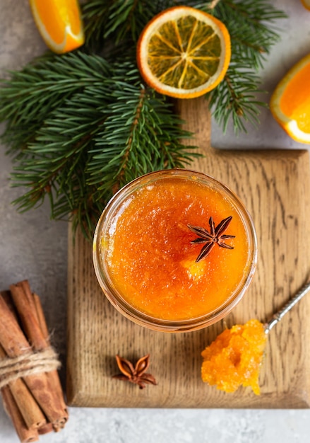 Orange jam in a glass jar with winter spices and fir branches.