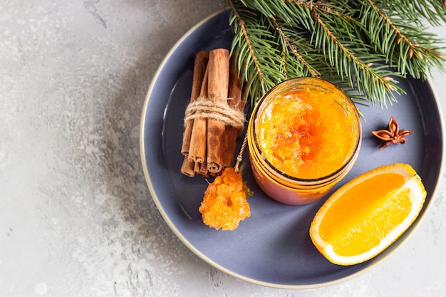 Orange jam in a glass jar with winter spices and fir branches.