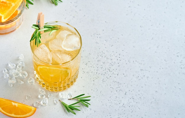 Orange juice or cocktail with rosemary and orange with ice in glass, cold summer lemonade on light gray slate, stone or concrete background. Beach concept with deep sun shadow. Top view.