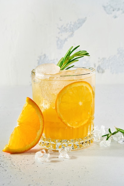 Orange juice or cocktail with rosemary and orange with ice in glass, cold summer lemonade