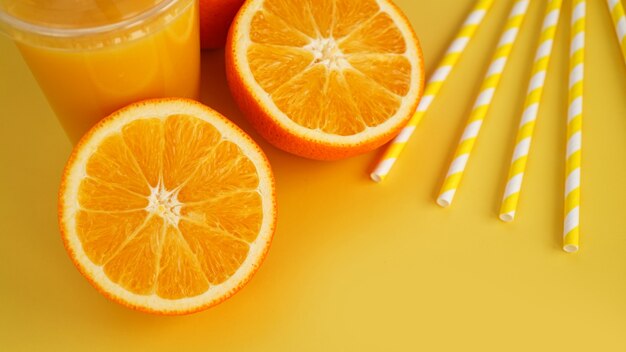 Апельсиновый сок в закрытой чашке быстрого питания с трубкой на желтом фоне. Нарезанные оранжевые и желтые бумажные соломинки для напитка