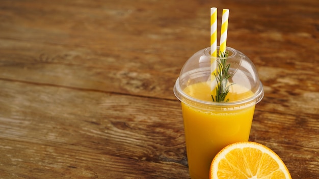 Orange juice in fast food closed cup with tubes on wooden table Fresh summer drink