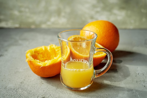 絞りたてのオレンジの皮の横にあるグラスに入ったオレンジジュースシンプルで生の食品