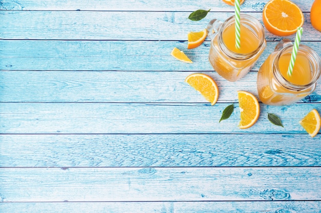 orange juice in glass jars and fresh oranges on a blue background.
