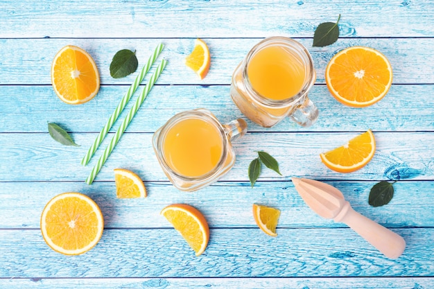 Orange juice in glass jars and fresh oranges on a blue background.