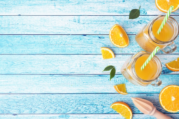 orange juice in glass jars and fresh oranges on a blue background.