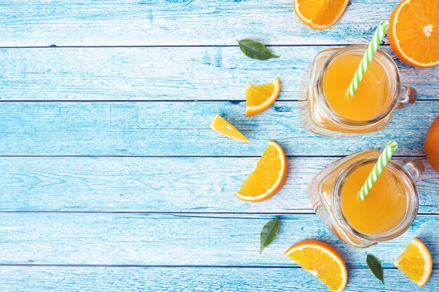 Orange juice in glass jars and fresh oranges on a blue background.