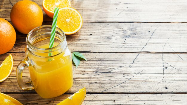 Orange juice in glass jars and fresh oranges on a wooden rustic table. Copy space.