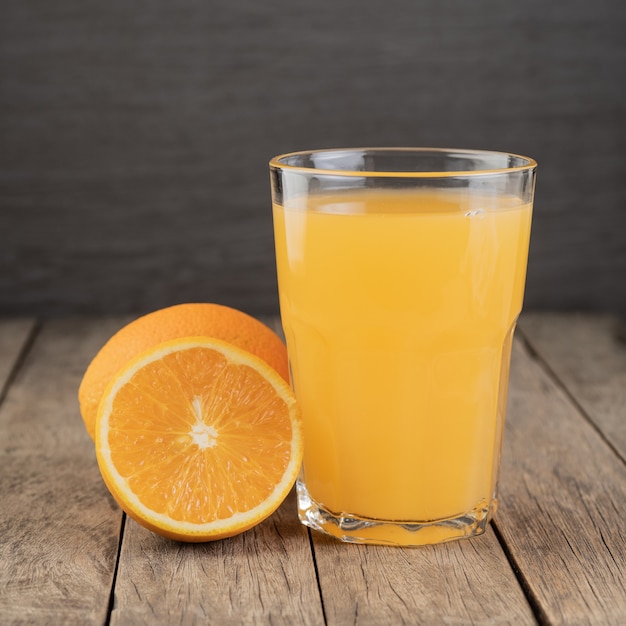 Foto succo d'arancia in un bicchiere con frutta sul tavolo di legno.