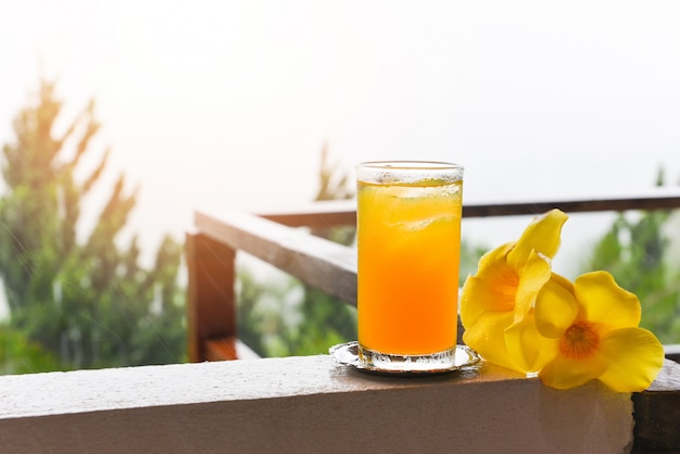 Стакан апельсинового сока с желтым цветком на балконе с каплями дождя утром