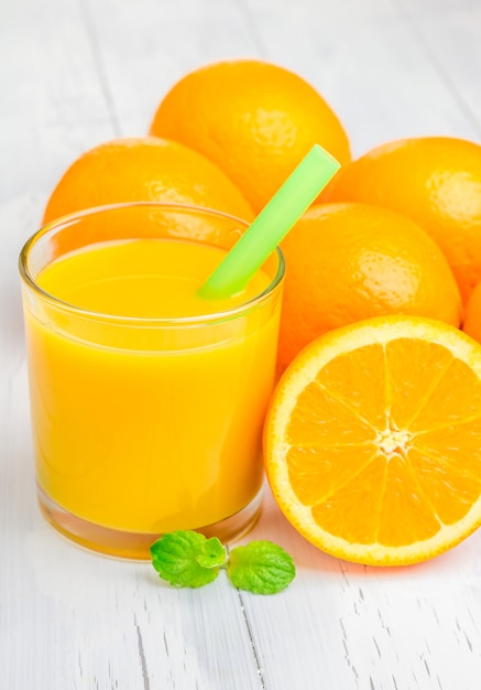 Orange juice and oranges with mint on white table