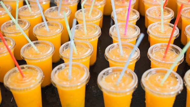 An orange juice in the plastic disposable cup with straws