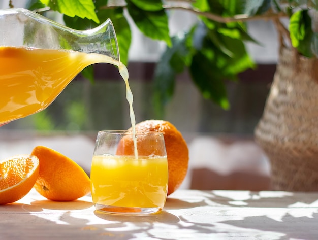 Orange juice pouring from pitcher into glass Healthy citrus drink Summer freshness concept