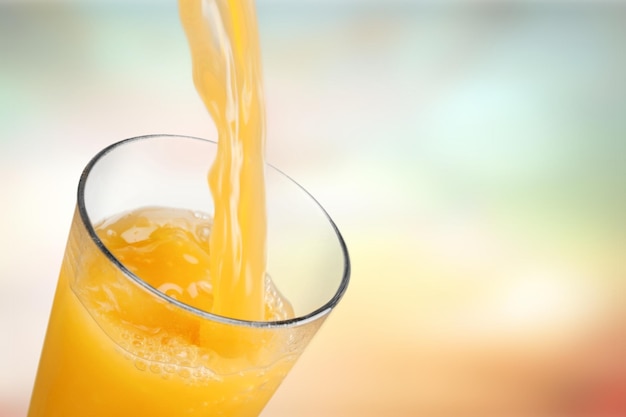 Orange juice pouring in glass on background