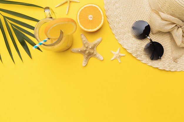 Orange juice starfish hat and sunglasses on yellow background with copy space top view