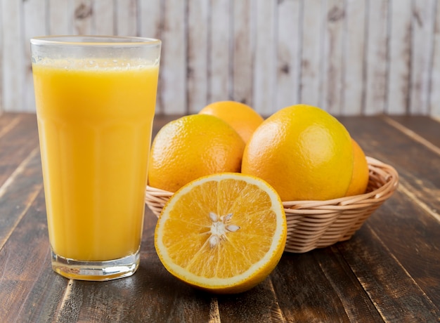 Orange juice with oranges in a basket and cut fruit over wooden table.