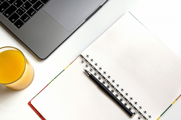 Photo orange juice on workplace. laptop, glass of orange juice and notebook on white desk.