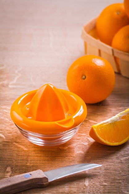 Orange juicer and fruits with kitchen knife on wooden board