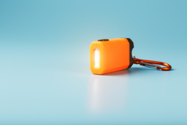 Photo an orange led flashlight with a carabiner glows on a blue background.