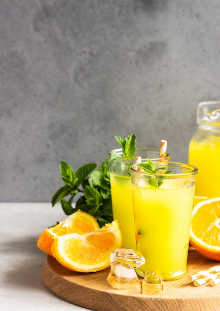 Orange lemonade in glass with fresh orange and mint over light grey stone table. Refreshing summer drink. Cocktail bar