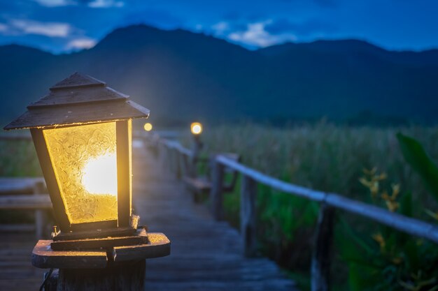 写真 朝の時間で古いランプからオレンジ色の光が男と山の背景に立つ