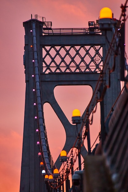 Orange lights in detail on support wires of American bridge with golden light behind