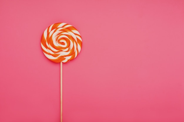 Orange lollipop on a pink surface