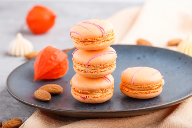 Orange macarons or macaroons cakes on blue ceramic plate . side view