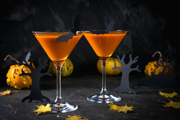 Orange martini cocktails with bats and decor for Halloween party, on dark background