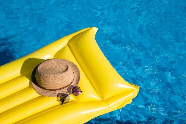 Materasso arancione in una piscina con cappello e occhiali da sole