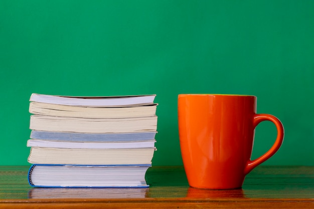 Tazza arancione con una pila di libri sul tavolo rustico e sfondo verde