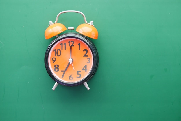 Orange old alarm clock on green background