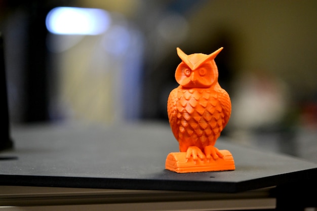 Orange owl object printed by d printer stands on blurry dark background