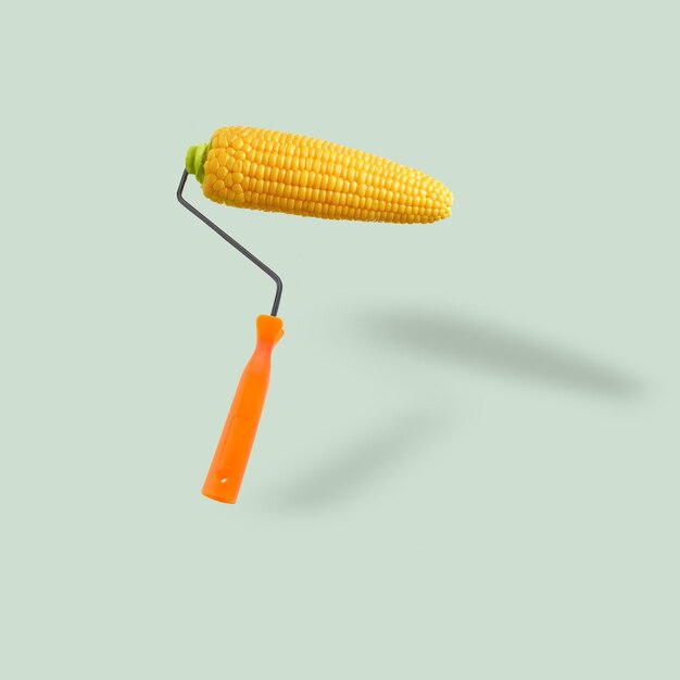 Photo orange paint roller as an fresh corn cob flying on pastel blue background.