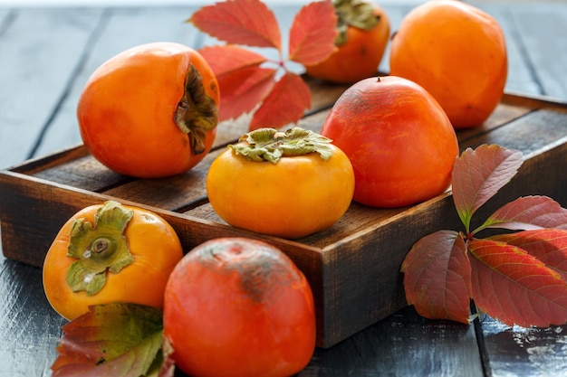 Orange persimmon and autumn leaves on wooden box