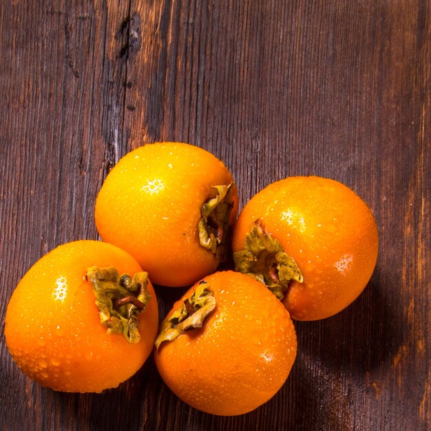 Orange persimmon fruits with water drops on a wooden background close-up copy space