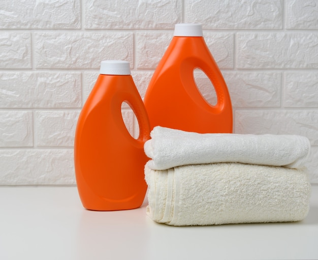 Orange plastic bottle of liquid washing powder and folded towels on a white shelf