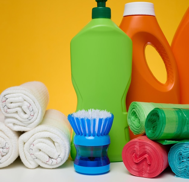 Orange plastic bottles with liquid products and garbage bags brushes and textile rags for washing floors on a white table