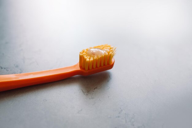 Orange plastic toothbrush with toothpaste on gray cement table. Dental clinic banner design