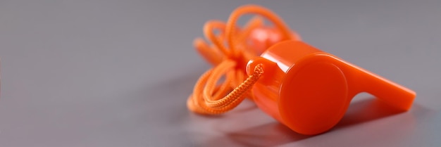 Orange plastic whistle with rope on gray background