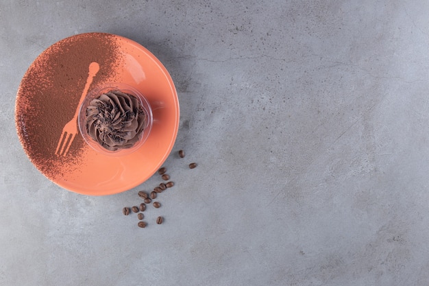 An orange plate with chocolate creamy cupcake and coffee beans . 