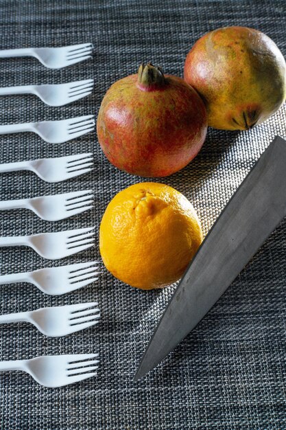 Orange pomegranate fruits placed on a table mat with fruit fork and knife