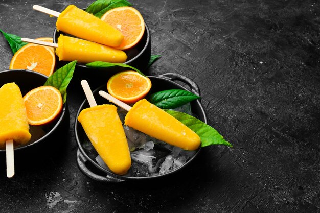 Orange popsicles on ice Cold summer fruit sweets On a stone background