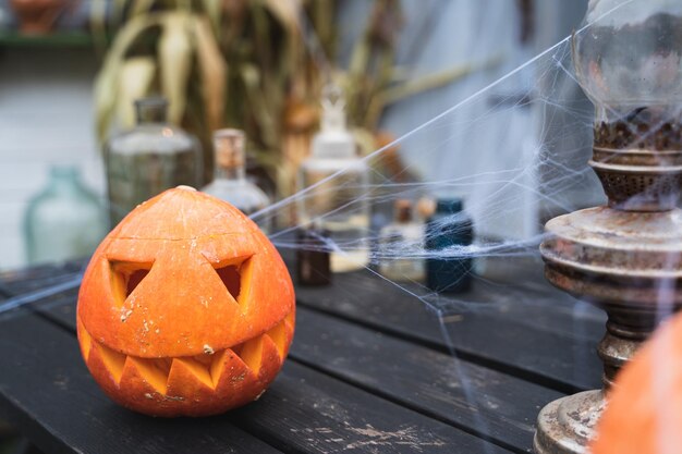 Orange pumpkin for halloween jackolantern with scary carved eyes mouthCandles old lamp spiderweb on wooden table near barn DIY homestreet decoration entertainment for children horror